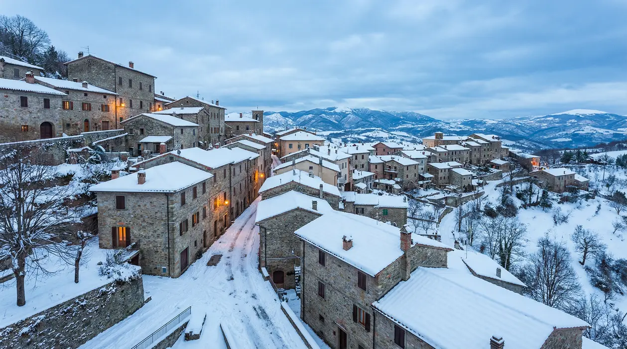 Borgo di montagna ricoperto di neve durante l'inverno con case in pietra e paesaggio collinare