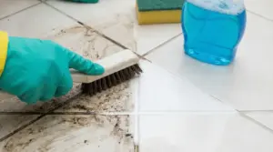 Mano con guanto che pulisce le fughe sporche del pavimento con una spazzola